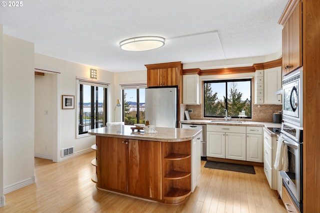 kitchen with light wood-type flooring, stainless steel appliances, decorative backsplash, a kitchen island, and sink