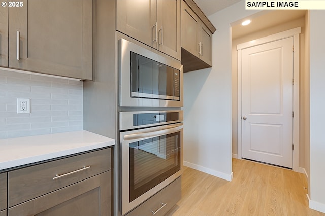 kitchen with tasteful backsplash, light countertops, light wood-style floors, stainless steel oven, and built in microwave