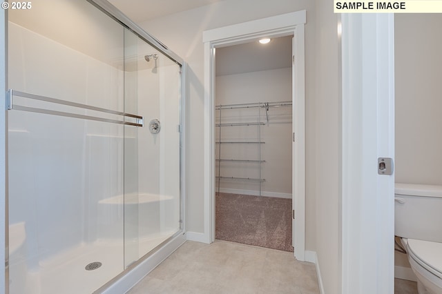 bathroom with a spacious closet, a stall shower, toilet, and baseboards