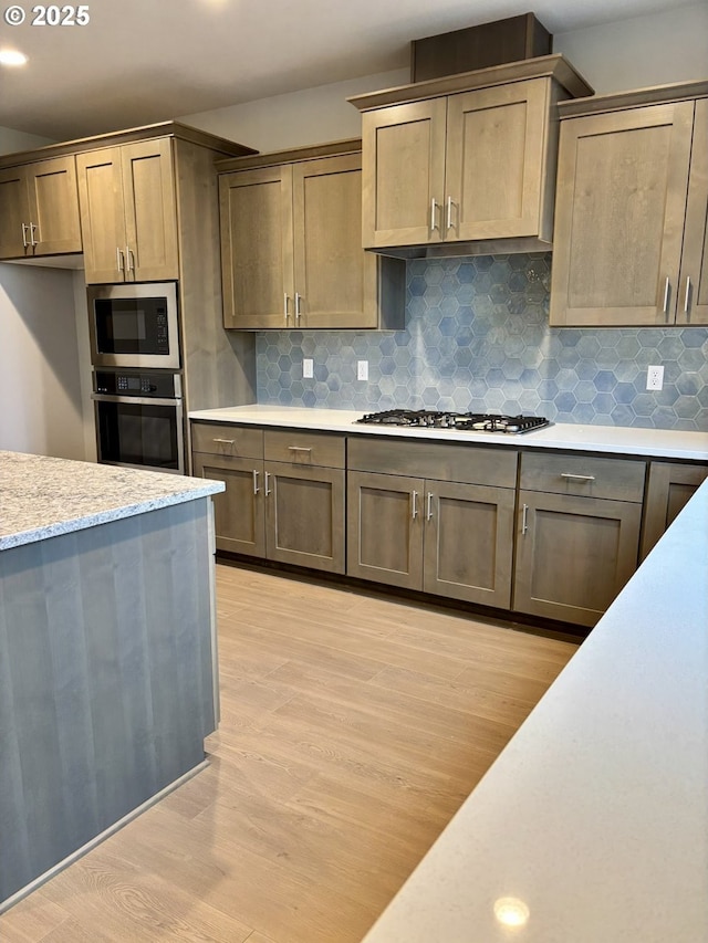 kitchen featuring stainless steel appliances, light wood-style floors, backsplash, and light stone countertops