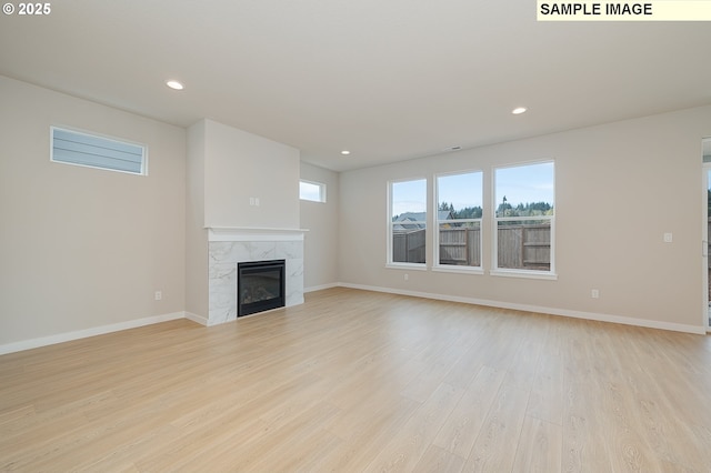 unfurnished living room with light wood finished floors, recessed lighting, baseboards, and a high end fireplace