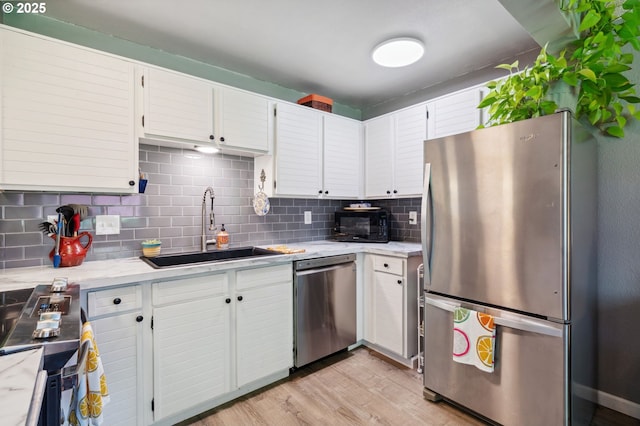 kitchen featuring decorative backsplash, white cabinets, a sink, light wood-style flooring, and stainless steel appliances