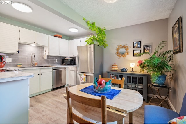 kitchen featuring stainless steel appliances, decorative backsplash, a sink, and light wood finished floors
