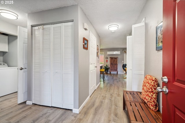 corridor with light wood-type flooring, a textured ceiling, washer / dryer, and an AC wall unit