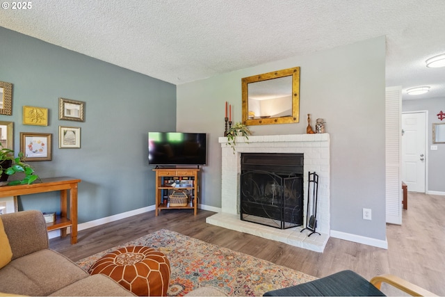 living area featuring baseboards, a textured ceiling, wood finished floors, and a fireplace
