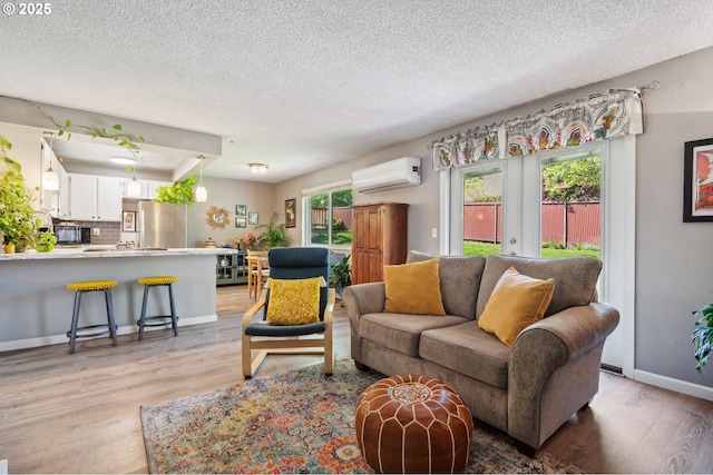 living area with baseboards, a wall unit AC, a textured ceiling, and light wood-style flooring