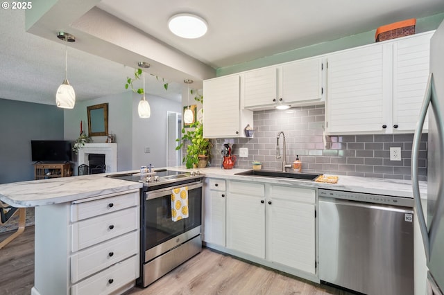 kitchen featuring backsplash, appliances with stainless steel finishes, a sink, light wood finished floors, and a peninsula