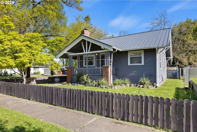 view of front facade featuring metal roof, a porch, fence private yard, a chimney, and a front yard