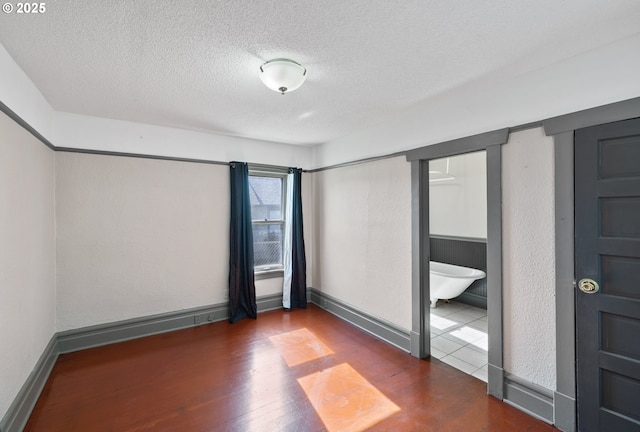 spare room with dark wood-style flooring, a textured ceiling, and baseboards