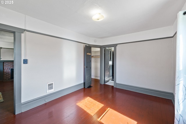 empty room with baseboards, a fireplace, visible vents, and dark wood-type flooring