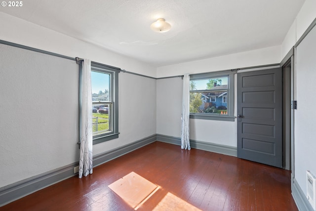 unfurnished room with a healthy amount of sunlight, baseboards, and dark wood-type flooring