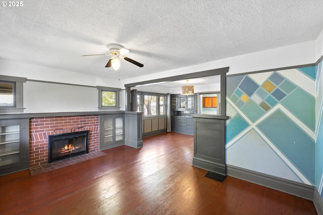 unfurnished living room featuring dark wood-style floors, a brick fireplace, a textured ceiling, and a ceiling fan