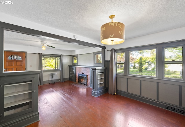 unfurnished living room featuring dark wood-type flooring, a fireplace, a textured ceiling, and ceiling fan