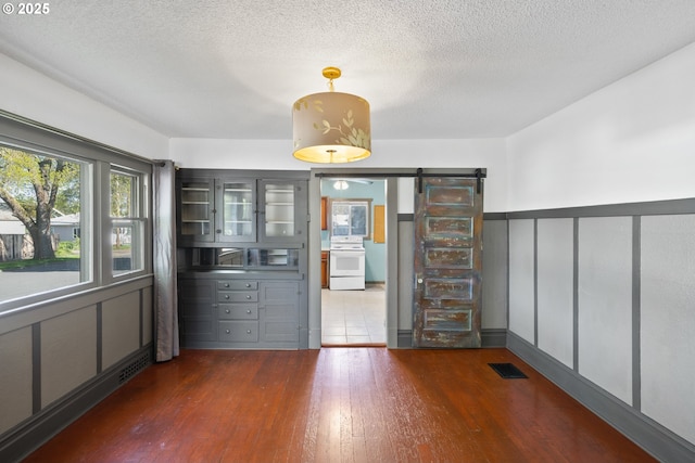 unfurnished dining area with dark wood-style flooring, visible vents, a barn door, wainscoting, and a textured ceiling