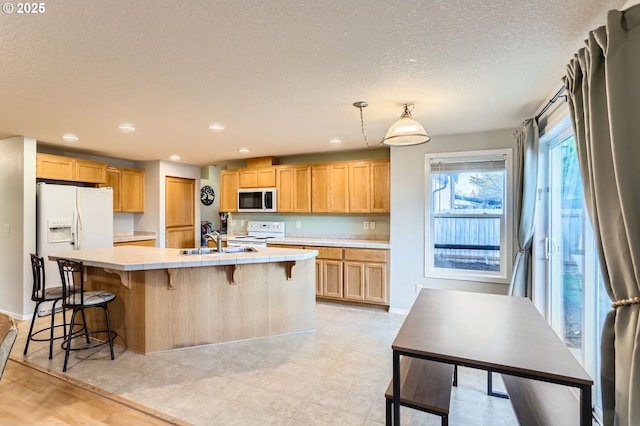 kitchen with white appliances, a spacious island, a sink, and light brown cabinetry