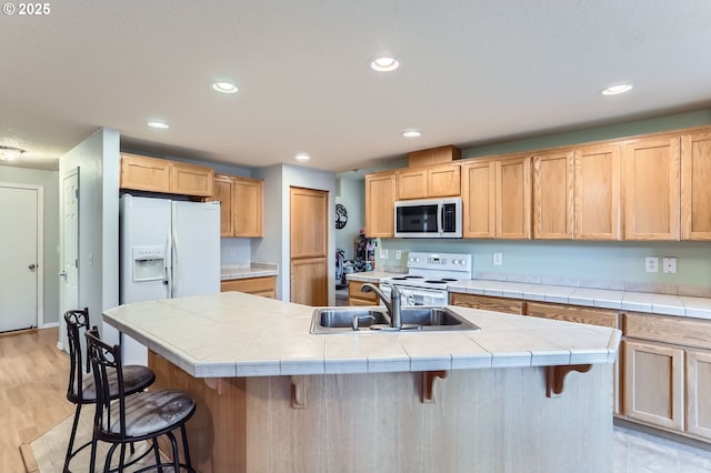 kitchen with light brown cabinetry, white appliances, a sink, and a kitchen breakfast bar