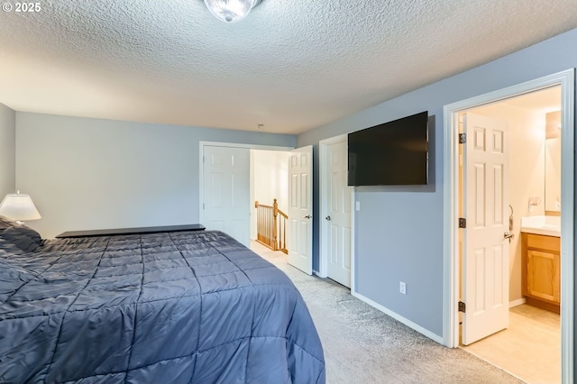 bedroom featuring light carpet, connected bathroom, baseboards, and a textured ceiling