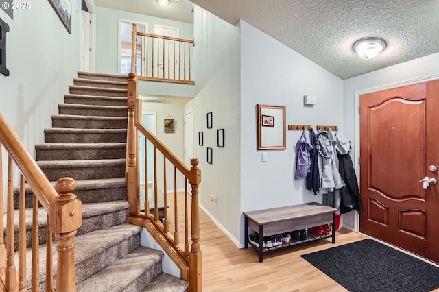 foyer entrance featuring a textured ceiling, stairway, light wood-style flooring, and baseboards