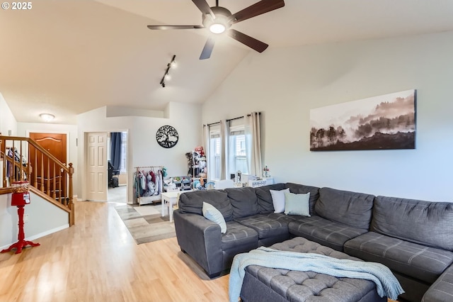 living area with stairway, light wood-style floors, a ceiling fan, high vaulted ceiling, and baseboards