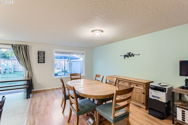 dining space with light wood-style flooring, baseboards, and a textured ceiling