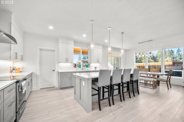 kitchen featuring stainless steel electric range, a breakfast bar, light countertops, and light wood-style floors