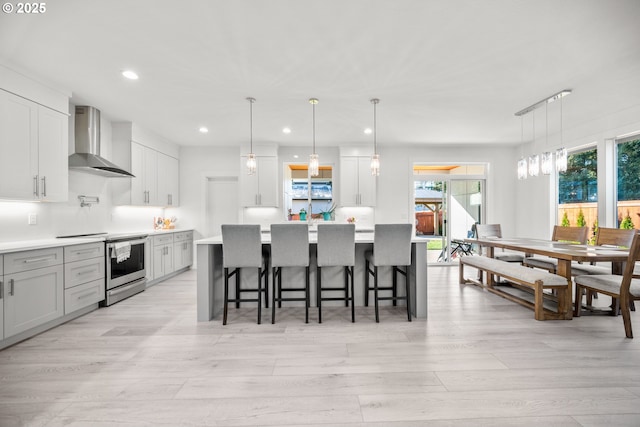 kitchen featuring a breakfast bar area, light wood finished floors, light countertops, electric stove, and wall chimney exhaust hood