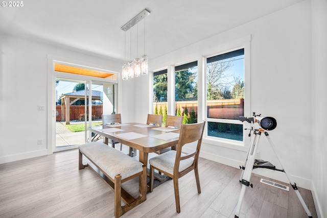 dining area with light wood finished floors, a notable chandelier, visible vents, and baseboards