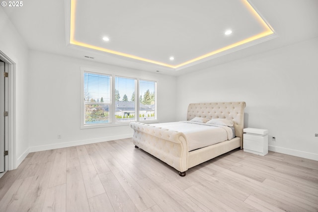 bedroom with baseboards, light wood-style floors, and a tray ceiling