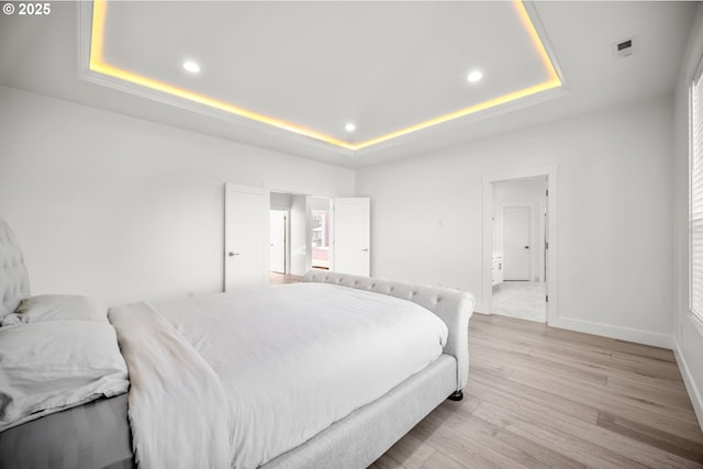 bedroom with recessed lighting, baseboards, light wood-style floors, and a tray ceiling