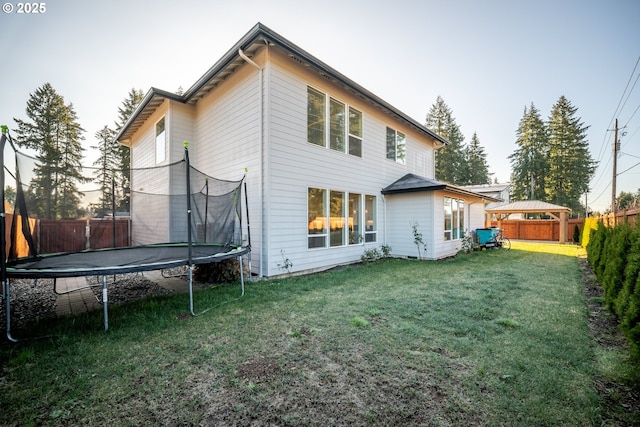 back of property with a yard, a trampoline, and a fenced backyard