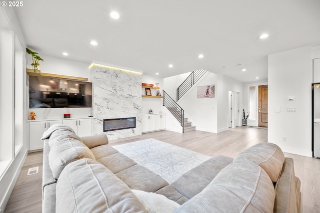 living room with light wood finished floors, visible vents, a high end fireplace, stairway, and recessed lighting