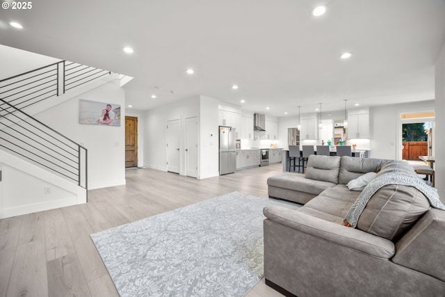 living area featuring recessed lighting, stairway, baseboards, and light wood-style flooring