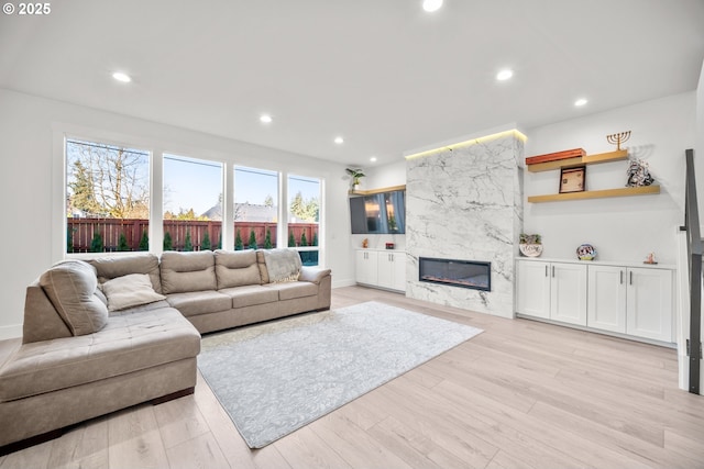 living area featuring recessed lighting, a premium fireplace, baseboards, and light wood finished floors