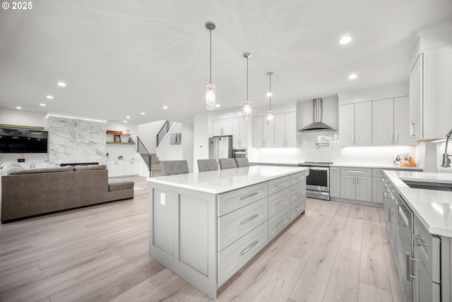 kitchen featuring gray cabinetry, wall chimney range hood, light wood finished floors, stainless steel electric range oven, and light countertops