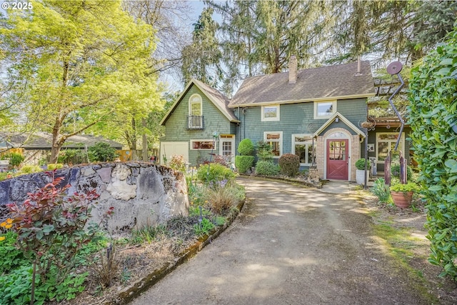 view of front of house with a shingled roof, a chimney, and driveway