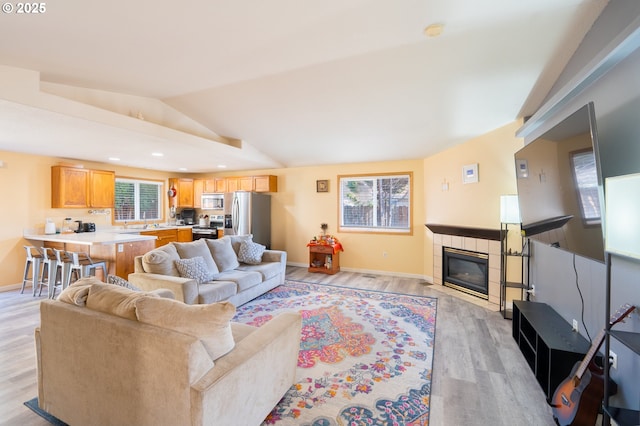 living area featuring lofted ceiling, recessed lighting, a tiled fireplace, light wood-style floors, and baseboards