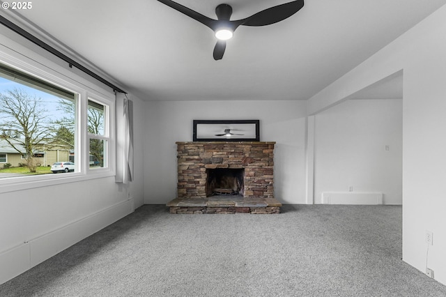 unfurnished living room featuring carpet, a stone fireplace, and a ceiling fan