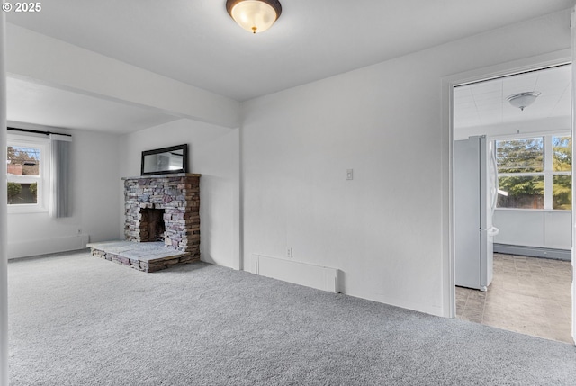 unfurnished living room featuring a stone fireplace, carpet, and a baseboard radiator