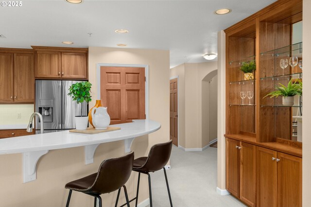 4873 NW Promenade Ter Unit 122, Portland, OR 97229 - kitchen featuring stainless steel fridge, a kitchen breakfast bar, recessed lighting, light colored carpet, and brown cabinets
