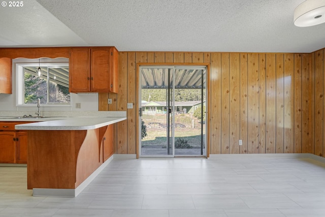 kitchen with sink, kitchen peninsula, a textured ceiling, and wood walls