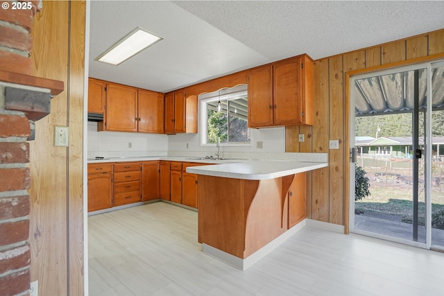 kitchen with sink, wood walls, a textured ceiling, and kitchen peninsula