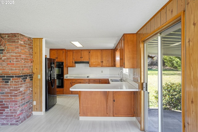 kitchen with wood walls, black appliances, sink, kitchen peninsula, and a textured ceiling