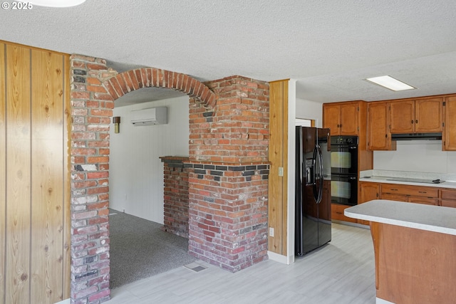 kitchen featuring a fireplace, a wall mounted AC, black appliances, a textured ceiling, and light wood-type flooring