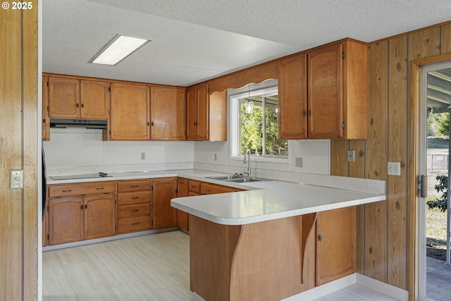 kitchen featuring wooden walls, sink, black electric stovetop, kitchen peninsula, and a textured ceiling