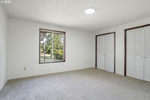 unfurnished bedroom with a textured ceiling, multiple closets, and carpet