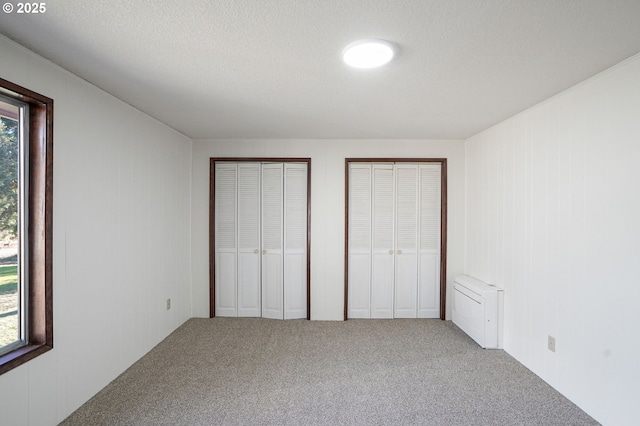 unfurnished bedroom featuring multiple closets, carpet flooring, and a textured ceiling