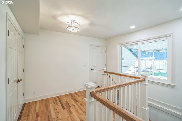 hall with an upstairs landing, light wood-style flooring, baseboards, and recessed lighting