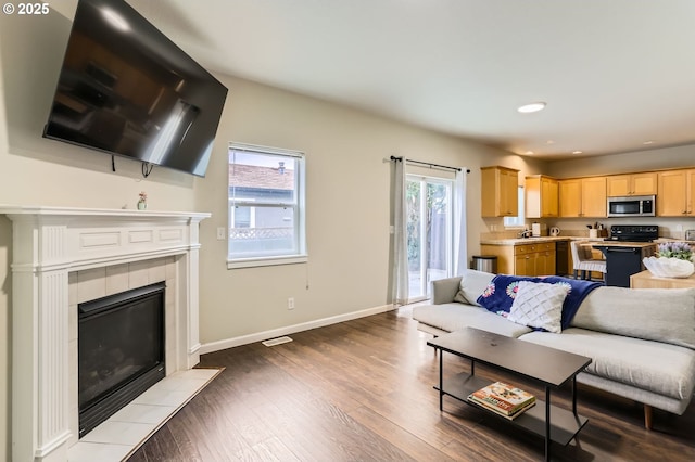 living room with plenty of natural light, baseboards, dark wood-style flooring, and a tile fireplace