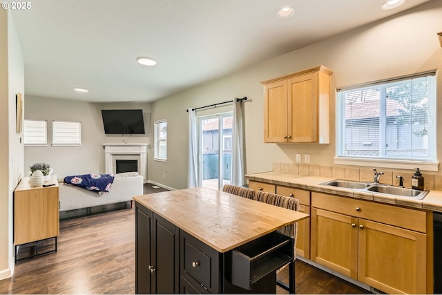 kitchen featuring a fireplace, tile countertops, recessed lighting, light brown cabinets, and a sink