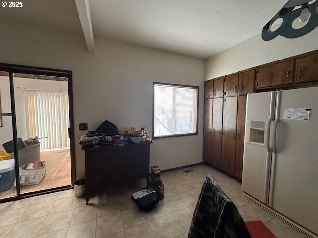 kitchen with white refrigerator with ice dispenser, dark brown cabinets, and beamed ceiling